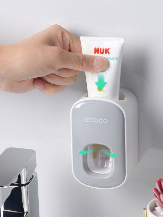 Hand using a NUK toothpaste tube with an ecoco dispenser on a light gray background